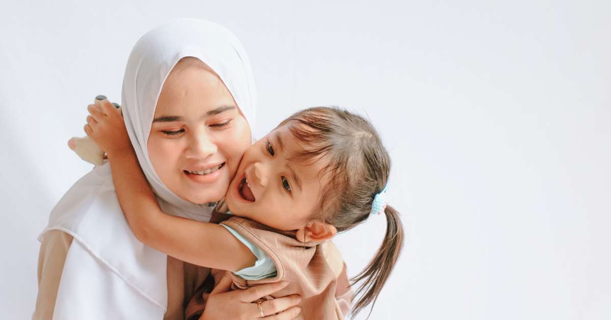 seorang ibu berhijab memeluk anak perempuan tersenyum bahagia 