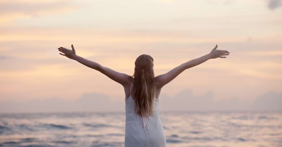 Seorang wanita merentangkan tangannya, bebas, bahagia di pinggir pantai (arti mimpi potong rambut)